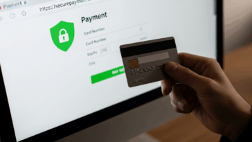 Main tenant une carte bancaire devant un écran affichant une page de paiement en ligne sécurisée avec cadenas et https visibles.